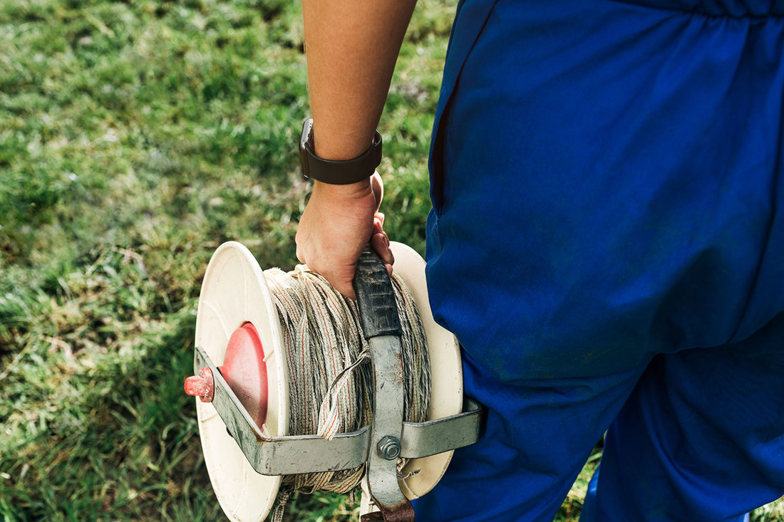 A dairy farmer standing in a paddock holding a reel of fencing tape